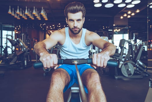 Feel his motivation. Front view of confident young man in sportswear doing rowing at gym and looking at camera photo