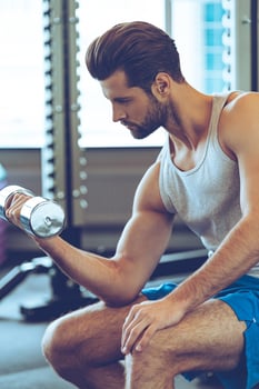 Nice burn in bicep. Side view of confident young handsome man in sportswear exercising with dumbbell at gym photo