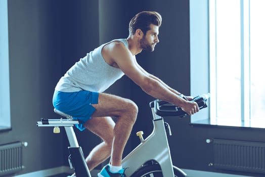 Workout with strength. Side view of young handsome man in sportswear cycling at gym photo