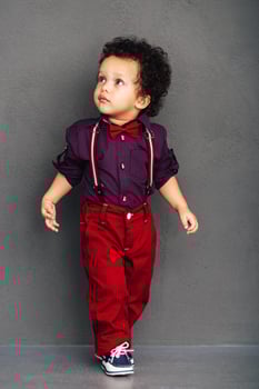 Like on catwalk. Little African baby boy looking away while walking against grey background photo