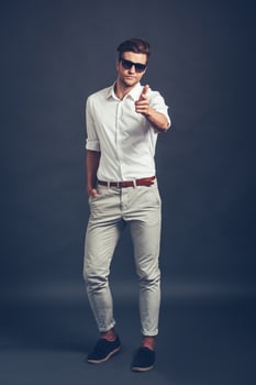 Maybe you Full length of confident young handsome man in sunglasses pointing you and looking at camera while standing against grey background photo