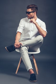 Mr Confidence. Full length of confident young handsome man in sunglasses looking away while sitting in chair against grey background photo
