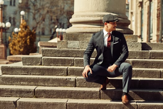 Portrait of retro 1920s english arabian business man wearing dark suit, tie and flat cap near old columns. photo
