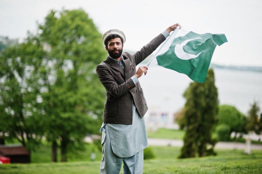 Beard pakistani man wear pakol hat and jacket hold Pakistan flag. photo