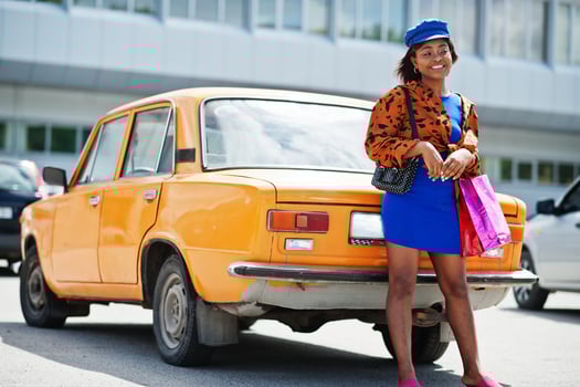 Beautiful african american lady with shopping bags standing near orange classic retro car. photo