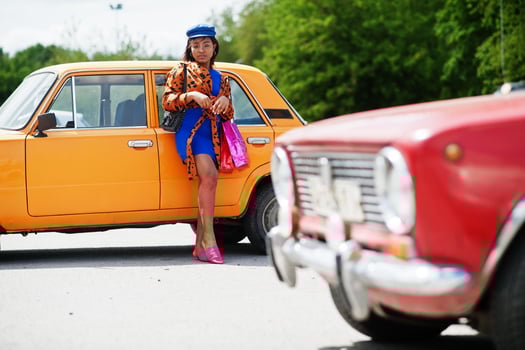 Beautiful african american lady with shopping bags standing near orange classic retro car. photo