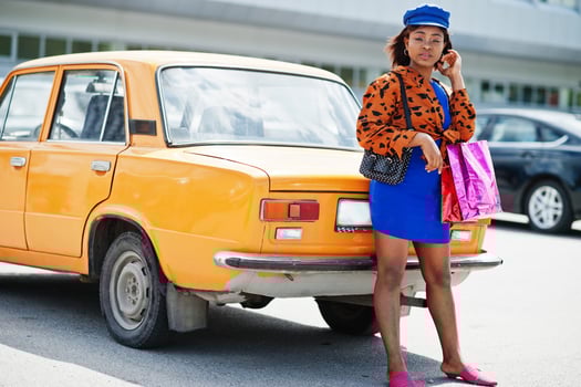 Beautiful african american lady with shopping bags standing near orange classic retro car. photo