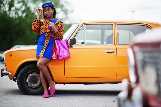 Beautiful african american lady with shopping bags standing near orange classic retro car. photo