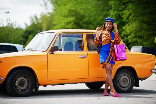 Beautiful african american lady with shopping bags standing near orange classic retro car. photo