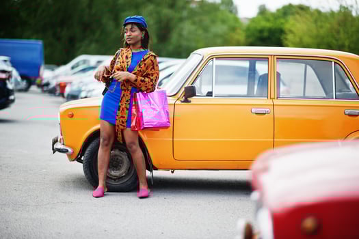 Beautiful african american lady with shopping bags standing near orange classic retro car. photo