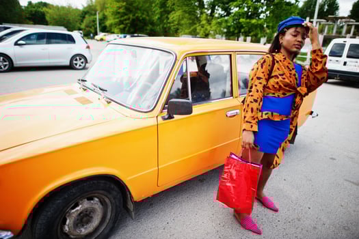 Beautiful african american lady with shopping bags standing near orange classic retro car. photo