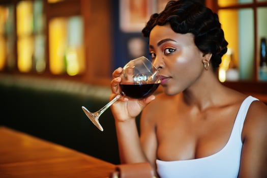 African american woman, retro hairstyle in white dress at restaurant with glass of wine. photo