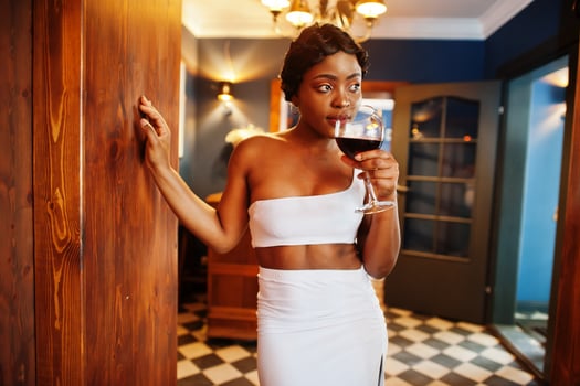 African american woman, retro hairstyle in white dress at restaurant with glass of wine. photo