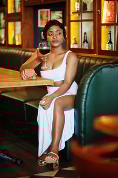 African american woman, retro hairstyle in white dress at restaurant with glass of wine. photo