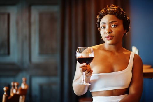African american woman, retro hairstyle in white dress at restaurant with glass of wine. photo