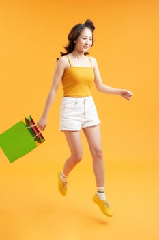 attractive happy smiling stylish woman shopaholic jumping running holding shopping bags on yellow background isolated photo