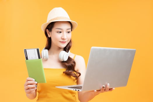 Tourist smiling girl holds passport in hand and looks at tickets on a laptop on a yellow background photo