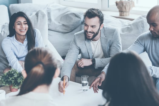 Making decisions together. Group of young business people discussing something while sitting together and pointing large blueprint laying on desk photo