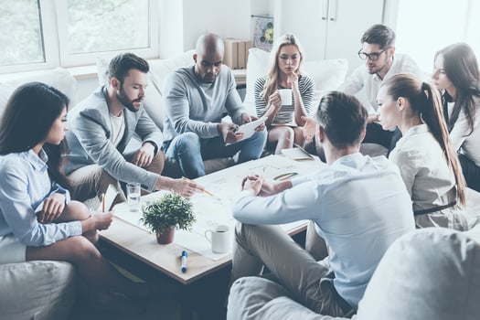 Discussing strategy. Group of confident business people discussing something while sitting around the desk together and pointing large paper laying on it photo