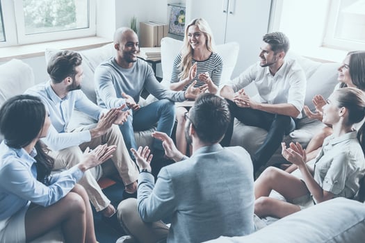 Applauding their achievements. Group of young cheerful people sitting in circle and applauding while one man gesturing and smiling photo