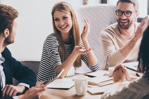 Sharing the latest news. Cheerful young people looking at each other with smile while sitting at the office table at the business meeting photo
