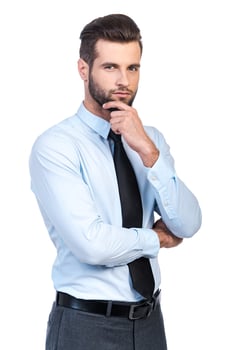 Thinking about solution. Thoughtful young handsome man in shirt and tie holding hand on chin and looking at camera while standing against white background photo
