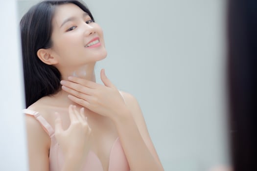 Beautiful sexy young asian woman looking mirror applying cream on neck and message, beauty girl applying body lotion skin care for health and soft hydration, treatment and cosmetic with moisturizer. photo