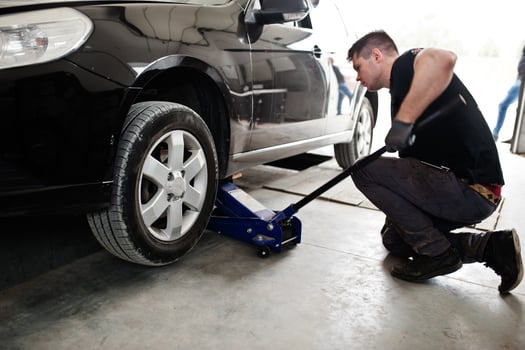 Car repair and maintenance theme. Mechanic in uniform working in auto service, lifted with hydraulic floor jack for repairing. photo