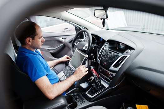 Car repair and maintenance theme. Electric mechanic in uniform working in auto service, making car diagnostics using obd device with laptop. photo
