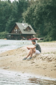 Inspiring with music and fresh air. Handsome young man in sports clothing wearing headphones and looking away while sitting on the riverbank photo