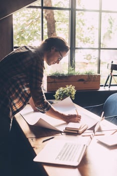 Working with passion. Confident young man in casual wear sketching on blueprint while standing near wooden desk in creative office photo