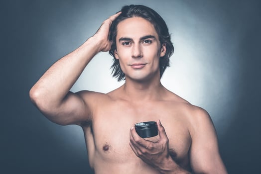 Used to look perfect. Portrait of young shirtless man looking at camera while applying hair gel and standing against grey background photo