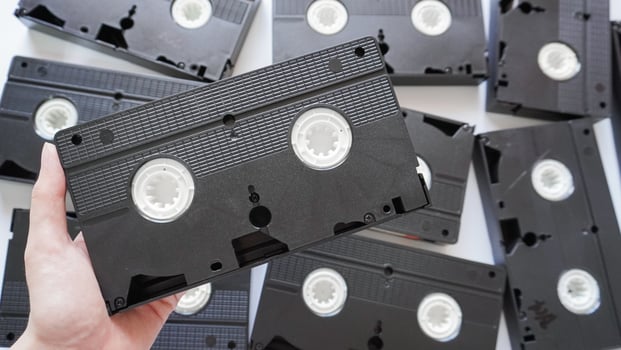 Hands holding a VHS tape back side with scattered tapes in the background. photo
