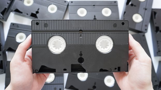 Hands holding a VHS tape back side with scattered tapes in the background. photo