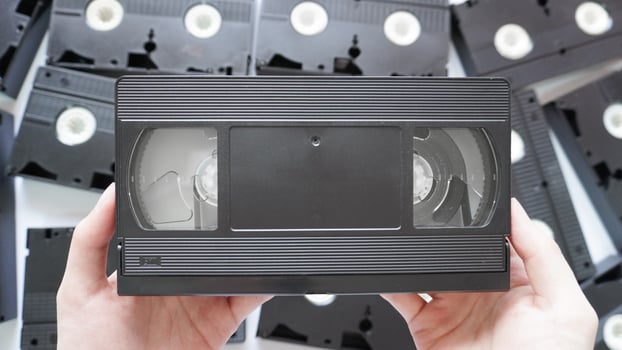 Hands holding a VHS tape back side with scattered tapes in the background. photo