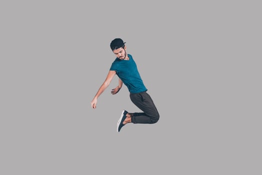 Carefree jumping. Mid-air shot of handsome young man in cap jumping and gesturing against background photo
