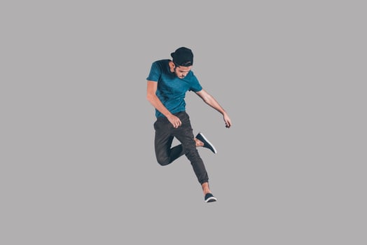 Young and cool. Mid-air shot of handsome young man in cap jumping and gesturing against background photo