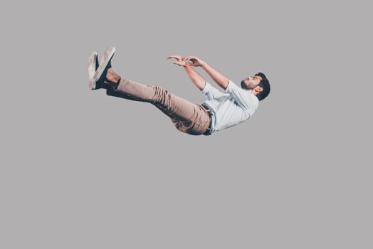 Just falling down. Mid-air shot of handsome young man falling against grey background photo