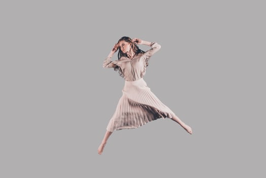 Jumping so high. Studio shot of attractive young woman in beautiful dress hovering in air photo