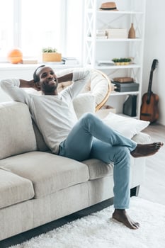 Lazy day at home. Handsome young African man holding hands behind head and smiling while sitting on the sofa at home photo