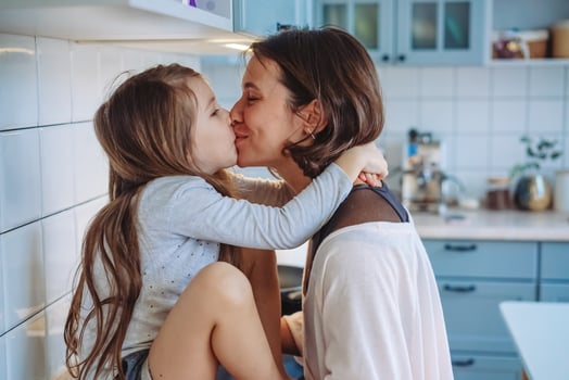 Mom kisses her little daughter in the kitchen photo