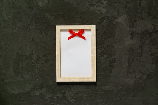 Wooden photo frame with red satin bow on black background. Mockup.