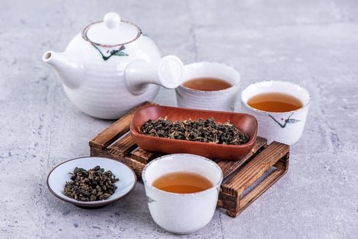 Hot tea in white teapot and cups on a sieve over bright gray cement background, closeup, copy space design concept. photo