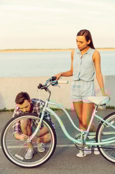 I can rely on him in any situation. Frustrated young women standing behind her bicycle while man repairing a wheel photo