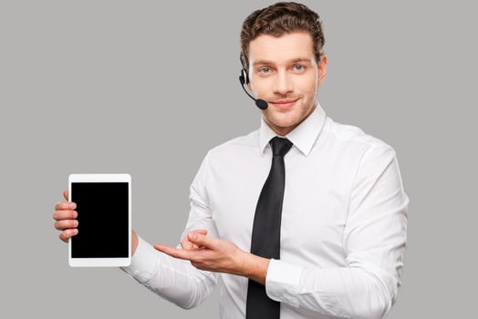 Copy space on his laptop. Handsome young man in formalwear and headset pointing  digital tablet while standing against grey background photo