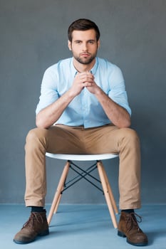 Smart and confident. Full length of handsome young man looking at camera while sitting against grey background photo