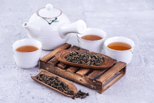 Hot tea in white teapot and cups on a sieve over bright gray cement background, closeup, copy space design concept. photo