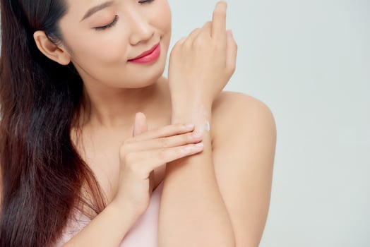 Smiling young woman applies cream on her hands. On a white background. photo