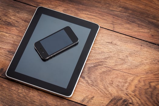 Multifunctional gadgets. Close-up of digital tablet with mobile phone laying on the wooden desk photo