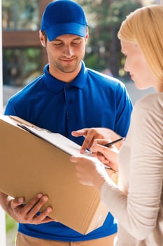 Just sign here. Handsome young delivery man holding a cardboard box while beautiful young woman putting signature in clipboard photo